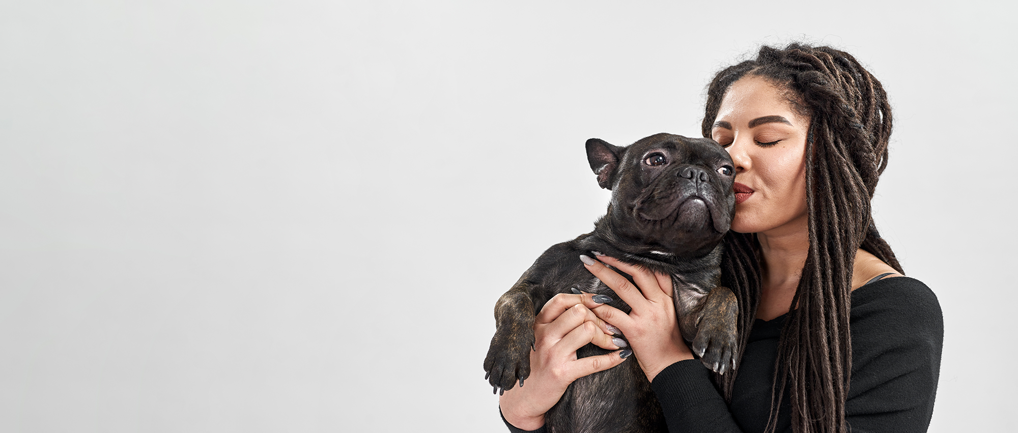 Woman with dreadlocks holding and kissing a black dog on a white background