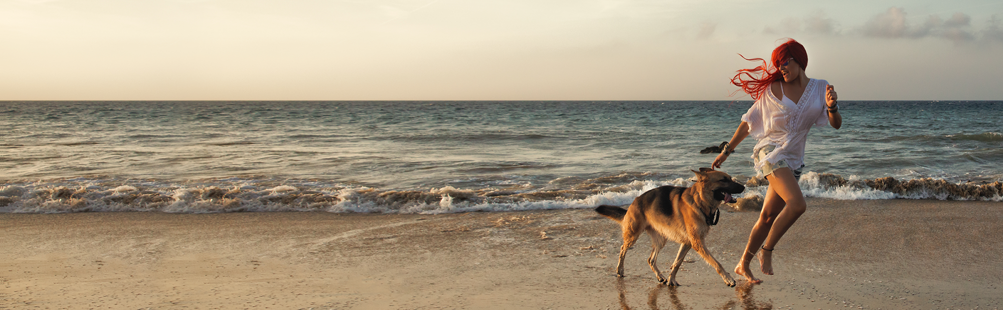 Woman running with a dog on a beach at sunset